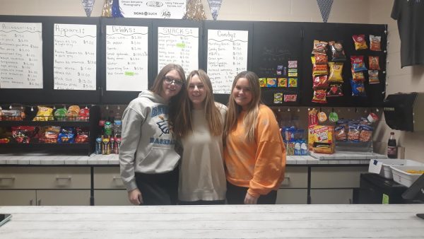 Three students who are working in the school store smile for the camera