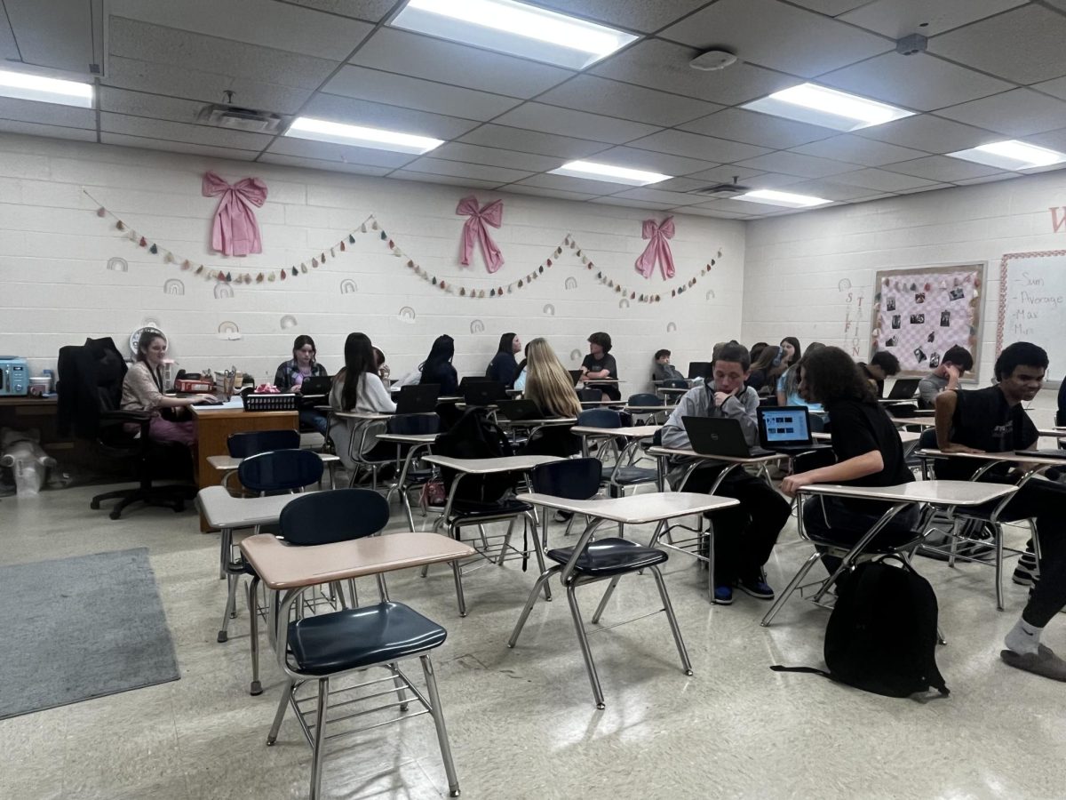 Students in Ms. Roberts' computer science class work on projects while she looks on. 